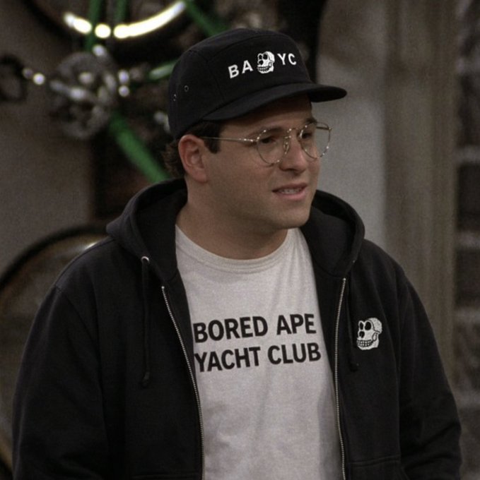 A man wearing a black cap reading "BAYC" and a white t-shirt with "BORED APE YACHT CLUB" printed on it, paired with a black hoodie featuring a small skull logo, looks off to the side with a slightly bewildered expression—perfectly capturing the caption "Who's +1 is this???"