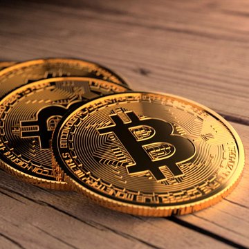 Two gold Bitcoin coins rest on a wooden surface, symbolizing the digital currency at the center of a story where a hacker stole $340M worth of Bitcoin by exploiting a bug and returned around 3,400 of the 4,000 stolen BTC after the vulnerability was patched.