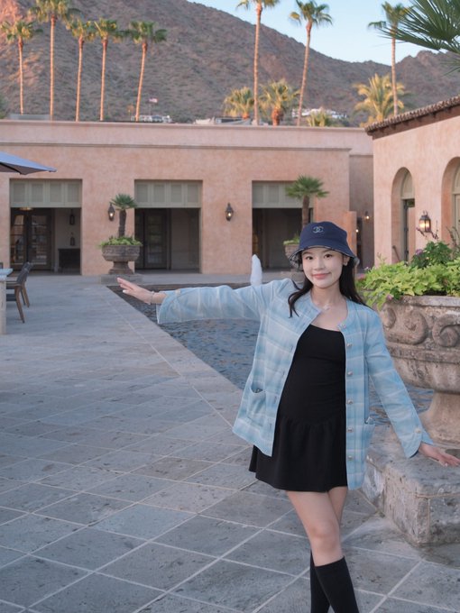 A young woman in a blue plaid shirt and Chanel bucket hat poses in a Spanish-style courtyard with palm trees and mountains in the background, capturing a relaxed, vacation-like vibe in what appears to be Palm Springs or a similar warm-weather locale.

The image conveys a leisurely weekend atmosphere that complements the post's invitation to gather with friends in Hong Kong for casual yet insightful discussions about startups, GTM strategies, and AI observations.