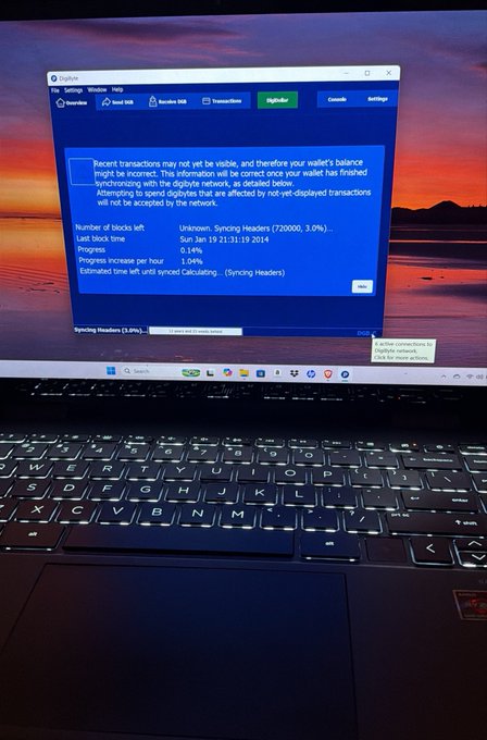 A photograph of a laptop screen displaying the Digibyte wallet 'Overview' page, showing blockchain sync information including 720,000 syncing headers at 3.0% progress.