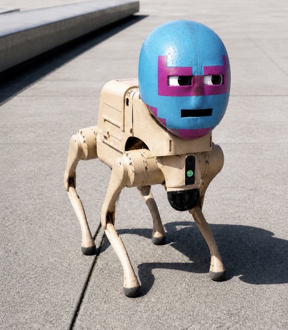 A quadrupedal robot dog with a wooden frame and a blue head featuring a pink cross design, standing on a concrete surface.