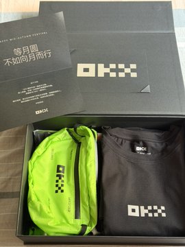 A black OKX branded gift box containing a neon green fanny pack and a black t-shirt, alongside a greeting card with Chinese text.