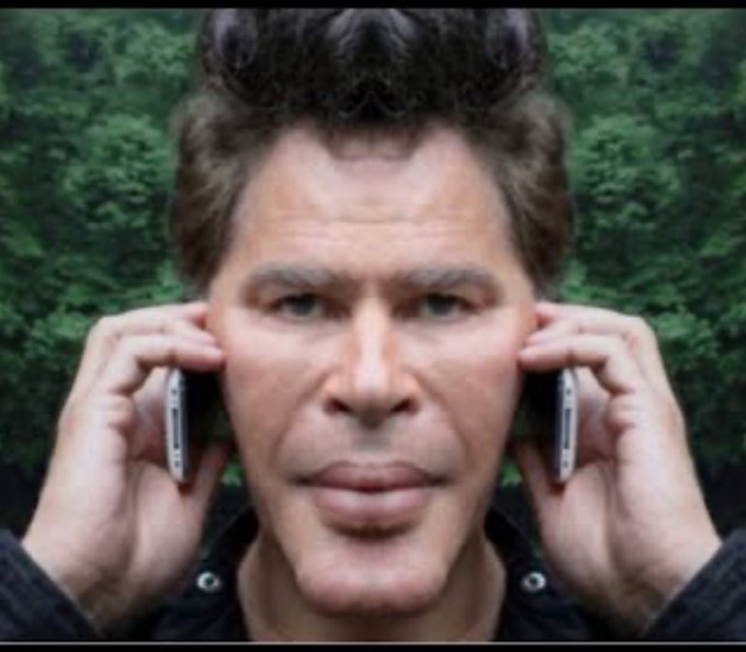 A close-up photo of a man holding two mobile phones, one against each side of his head, with a forest background.