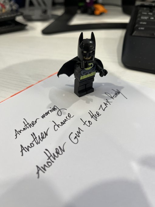 A Lego Batman minifigure standing on a piece of paper with the handwritten text 'Another morning, Another chance, Another Gin to the LN family'.