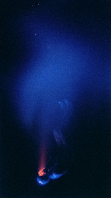 The image shows a pair of shoes with red lights on them, floating in space against a dark background. The shoes appear to be emitting a blue light from their soles, creating an interesting visual effect. The caption below the photo reads "Dropping the Anchor Only to Be Dragged Under 1/1 on TransientLabs 0.015 eth". This phrase is likely a reference to the image's title and could be related to the shoes' unique lighting feature or some other aspect of the scene.