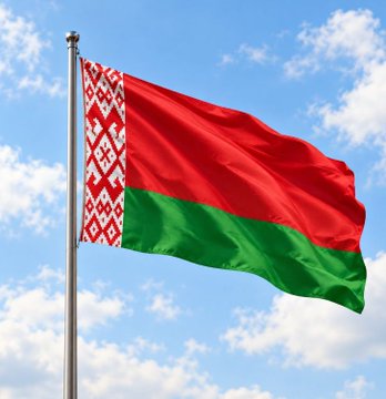 A waving flag of Belarus with its distinctive red and green horizontal stripes and red-and-white ornamental pattern on the hoist, set against a blue sky with scattered clouds.