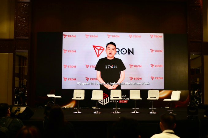 A speaker appears on a large screen at Indonesia Blockchain Week 2026 wearing a TRON-branded t-shirt, with the subtitle 'It's great to be back at Indonesia Blockchain Week' visible.