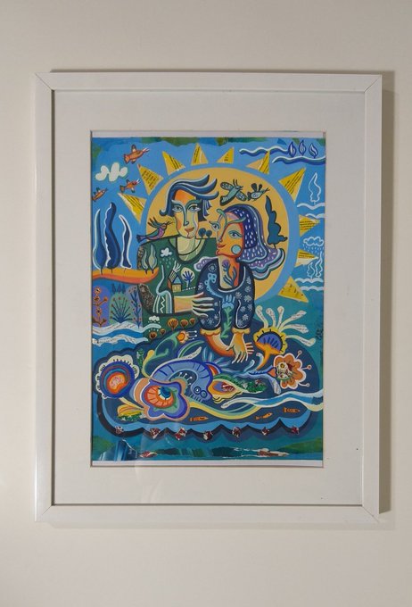 A framed colorful painting depicting two stylized figures embracing within a sun-like halo, surrounded by vibrant flora, birds, butterflies, and decorative patterns on a blue background.