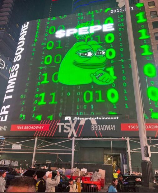 A large digital billboard at 1568 Broadway in Times Square displays a green Pepe the Frog with '$PEPE' text and binary code, shown on TSX.