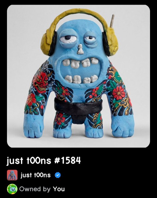 A blue clay monster figurine with a yellow antenna headband, sporting a tattooed body and an exposed-tooth grimace, displayed as "just t00ns #1584" NFT owned by the user. The image accompanies a giveaway announcement where the owner is celebrating a special day by raffling off this NFT to a community member.