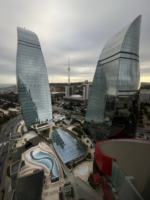 An aerial view of modern flame-shaped glass skyscrapers with a central TV tower in the background, likely in Baku, Azerbaijan.