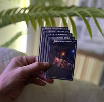 The image shows a person holding up five playing cards, each with a different scene or character on them. These cards are part of a tarot deck called "Moonbirds", which has been described as an expansion from the original deck. The cards feature various scenes and characters that may be interpreted in different ways depending on their context within the tarot reading.