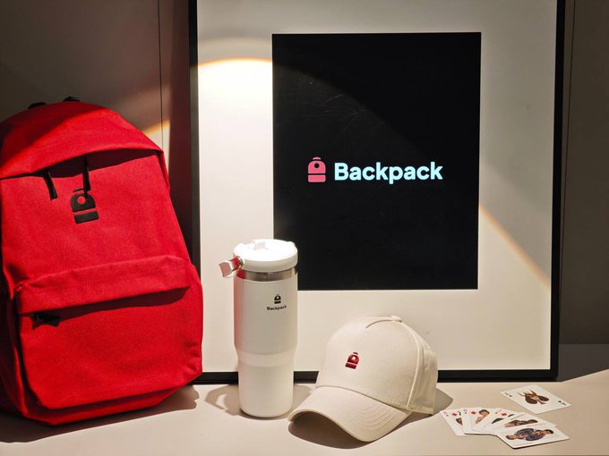 A product display featuring Backpack wallet branded merchandise: a red backpack, a white tumbler, a beige cap, and character stickers, with the Backpack logo displayed on a screen.