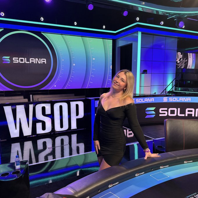 A woman in a black dress poses in front of a poker table setup with "WSOP" and "SOLANA" branding visible on the displays.