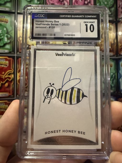 A hand holds a CGC (Certified Guaranty Company) graded card slab containing a 'VeeFriends Honest Honey Bee' card graded GEM MINT 10, signed in blue ink.