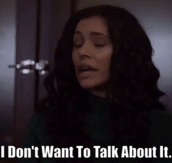 The image shows a woman with long, dark hair wearing a green shirt, looking at the camera while reading text that says "I don't want to talk about it." The background appears to be a room or hallway, but there are no other people or objects visible in the photo.