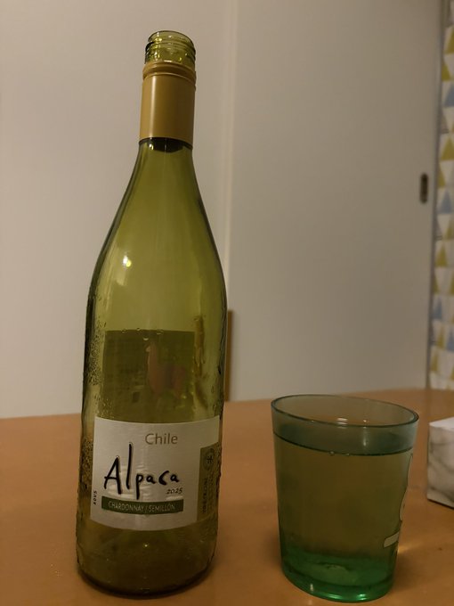 An empty bottle of "Chile Alpaca Chardonnay-Semillón 2020" wine sits next to a green drinking glass on a table, corresponding to the post's mention of enjoying a 600-yen bottle of Alpaca wine from 7-Eleven.