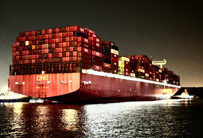 A nighttime photograph of the massive container ship 'ONE APUS' loaded with shipping containers on the water.
