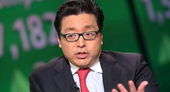 An Asian businessman in a suit and red tie gestures while speaking, photographed against a green background with numbers displayed.