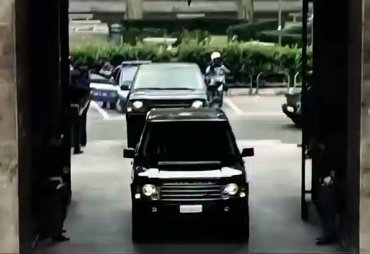 Security camera footage showing a dark SUV stopped at a gate with two figures in tactical gear standing near the vehicle in the background.