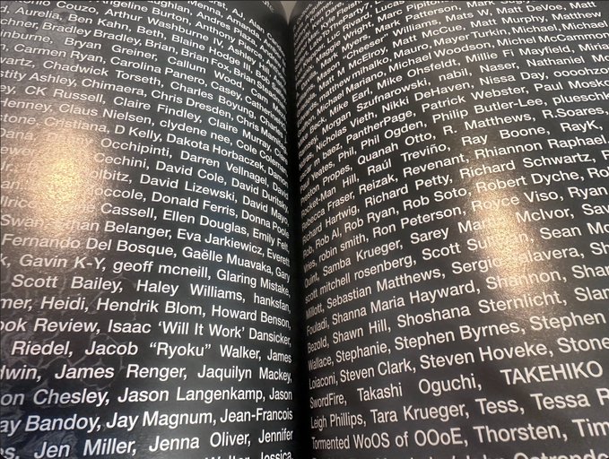 A close-up photograph of a dark book page densely printed with a long list of contributor names, including 'TAKEHIKO' visible near the bottom right.