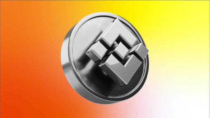 A silver metallic cryptocurrency coin with a geometric cube logo is displayed against a vibrant gradient background transitioning from orange to yellow.