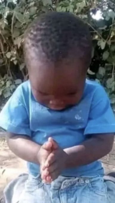 A young child wearing a blue shirt, with their head bowed and hands clasped together in a praying position.