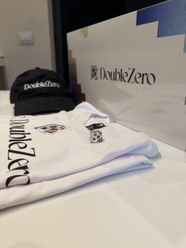 A display of merchandise featuring a black cap and a folded white shirt with the 'DoubleZero' logo, placed in front of a branded box.