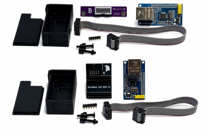 A collection of electronic components including two black plastic project enclosures, two Wemos D1 mini microcontrollers, two NerdQaxe LAN MOD V1 control boards, ribbon cables, and header pins laid out on a white surface.