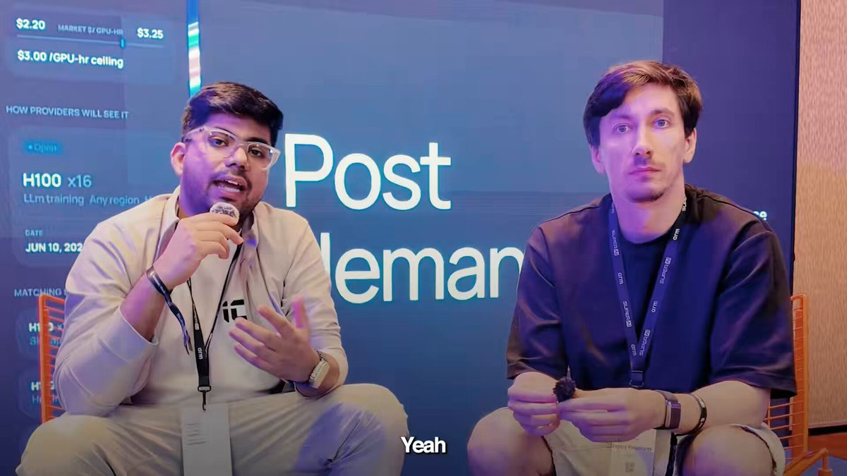 The image shows two men sitting next to each other, talking into microphones during a presentation or event. They are wearing name tags that say "Yeh" and "yeah", indicating they might be participating as speakers or presenters at the event. The background features a blue wall with white text on it, which is likely related to the post being discussed by the two men.