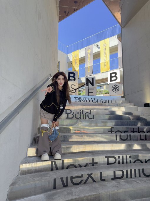 A woman posing on metal stairs featuring text including 'BNB CHAIN', 'Build', 'Next Billion', and 'for the'.