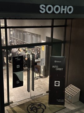 A view through a glass door into a modern space called 'SOOHO' with a black banner outside that reads 'Solanium INTO ORBIT'.