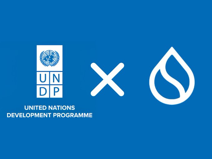 The image features a blue background with two white logos - one representing the United Nations (UN) and the other symbolizing a drop of water. The UN logo is positioned above the word "x", while the drop of water logo is below it. The text in the image reads, "United Nations x Development Programme". This suggests that there might be an association or collaboration between these two organizations, possibly related to sustainable development goals and initiatives.