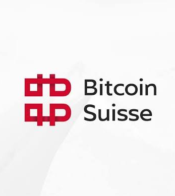 The Bitcoin Suisse logo, featuring a red stylized "B" symbol, is displayed on a white background. This logo corresponds to the Swiss cryptocurrency broker mentioned in the news about upcoming staff cuts of up to 30%.