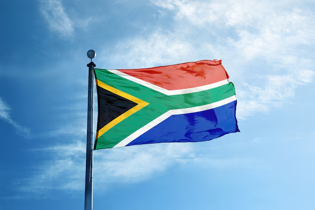 The South African flag waves against a blue sky, symbolizing the country's proposed regulations for cross-border crypto transfers. This imagery directly relates to the news of South Africa introducing new rules for handling crypto transactions, including those to offshore exchanges and self-custody wallets.