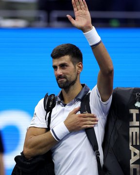 Tennis player Novak Djokovic waves while holding his racket bag after a match.