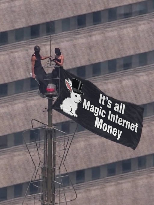 Two activists on a radio tower hoist a Playboy Bunny logo with the slogan 'It's all Magic Internet Money', referencing cryptocurrency in a Bitcoin-themed protest banner.