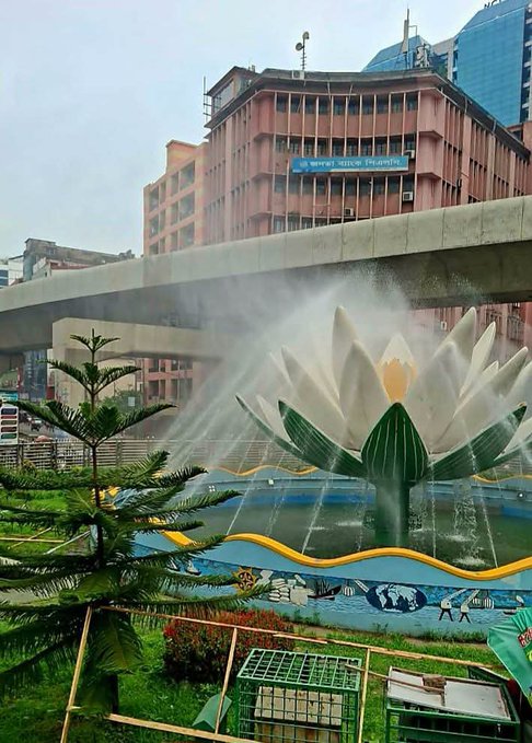 Photograph of a large lotus-shaped fountain in an urban Chinese city setting with a building displaying 'Summer Service' sign in the background.