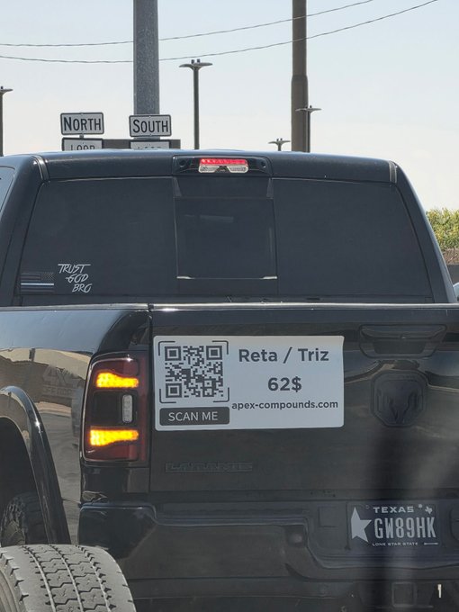 The image shows a black pickup truck with a white license plate that has a QR code on it, which reads "reta/triz 623". The back of the truck also features a sticker with the words "tell me we're early without telling me we're early" written in bold letters.

In addition to the truck and its stickers, there are two other cars visible in the image: one on the left side and another further away towards the right edge. The background of the image is filled with various street signs, including a "NORTH", "SOUTH", and "LONG HILLS" sign, as well as a "GNS89HK" sign.