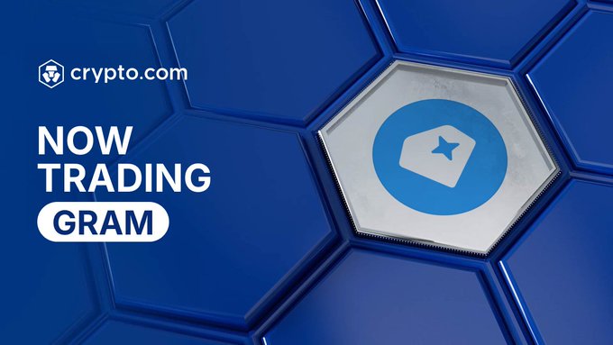 Crypto.com announces that Gram ($GRAM) is now trading, featuring the app's logo on a hexagonal blue background with "NOW TRADING GRAM" text alongside the Crypto.com branding.