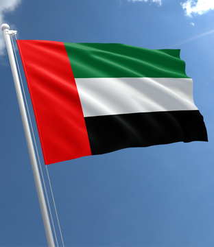 The image shows the flag of the United Arab Emirates, with its red vertical stripe and green, white, and black horizontal bands, waving against a blue sky. The flag visually represents the country where Kraken has just announced it will launch new cryptocurrency services, including dirham-denominated spot trading pairs.