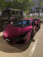 A sleek pink Lamborghini sports car is parked on a street, with a black off-road vehicle visible behind it, capturing the "showstopper" moment referenced in the post about it being the fastest car and a 1:1 scale model.