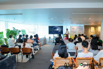 An indoor event photo with attendees seated facing a screen with the Aleo logo, watermarked 'Aleo OpenBuild'.
