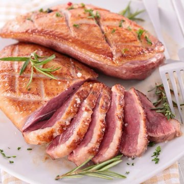 Two perfectly seared Muscovy duck breasts, sliced to reveal a juicy, pink medium-rare interior and garnished with fresh rosemary sprigs on a white plate, visually highlighting the rich, beef-like meat promoted in the post priced at $50.99 per 1.5-2 lbs with Bitcoin accepted.
