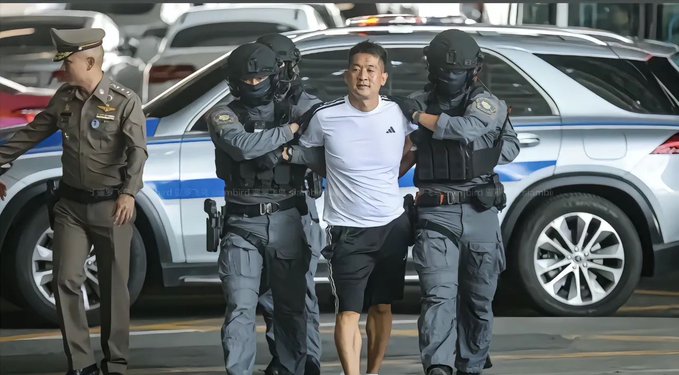 An unidentified man in a white t-shirt and black shorts is being escorted by multiple armed officers, likely related to a case or arrest. The image reflects the accompanying post's duality of public opinion towards a prominent figure: one side holding grudges, the other aspiring to emulate them.