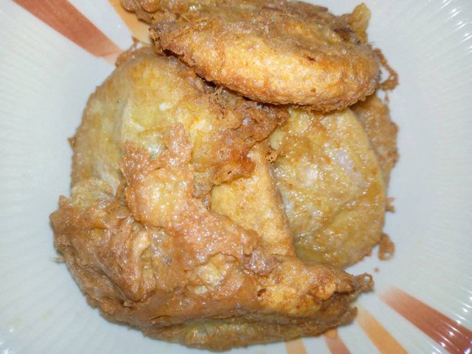 A close-up view of a golden-brown fried chicken portion, possibly a leg quarter, served on a white plate with a subtle patterned rim.