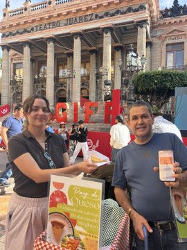 Two smiling cheesecake vendors stand in front of Guanajuato's Teatro Juárez, holding up their phones displaying a payment and a sign advertising "Pay de Queso" (cheesecake), successfully accepting a Monero ($XMR) payment through Cake Wallet after the seller finally agreed to the crypto transaction.