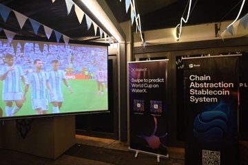 An indoor viewing area showing a football match on a large screen, with banners advertising 'Chain Abstraction Stablecoin System' and a 'Swipe to predict World Cup' promotion.