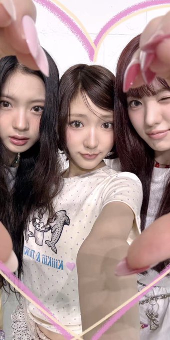 Three young women pose closely together for a selfie, framed by a digital pink heart filter.