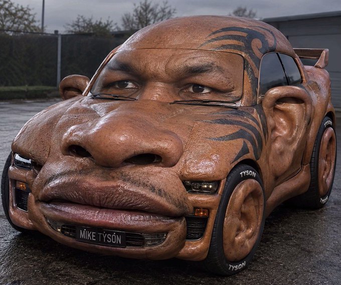 A surreal sculpted car designed to look like Mike Tyson's face, complete with tribal tattoos, featuring license plate 'MIKE TYSON' and 'TYSON' branded tires.